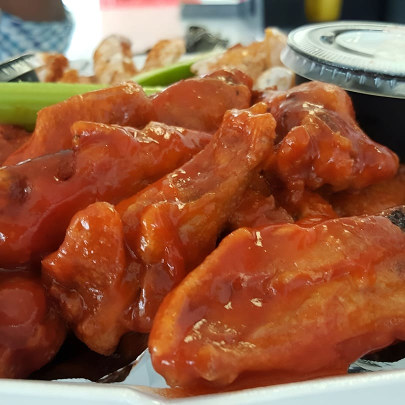 Close-up of WingOut Express's saucy, red-glazed chicken wings with celery sticks and dipping sauce.