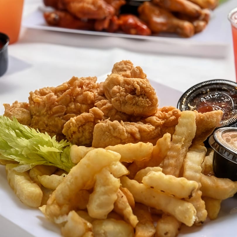 Crispy fried chicken tenders with crinkle-cut fries, celery, and dipping sauces on a white plate.