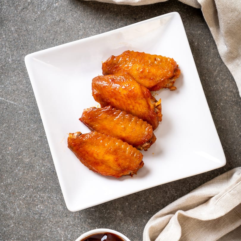 Five golden-brown, glazed WingOut Express chicken wings on a white rectangular plate.